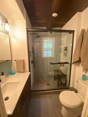 Frameless glass shower enclosure with black trim, white vanity, and dark ceiling in bathroom