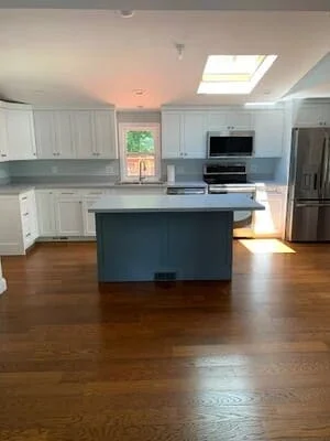 Modern kitchen with white cabinets, blue island, stainless appliances, and hardwood floors