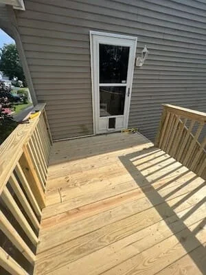 Newly constructed pressure-treated wood deck with railings and hot tub access door