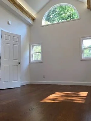 Empty room with hardwood floors, white door, arched window, and neutral walls