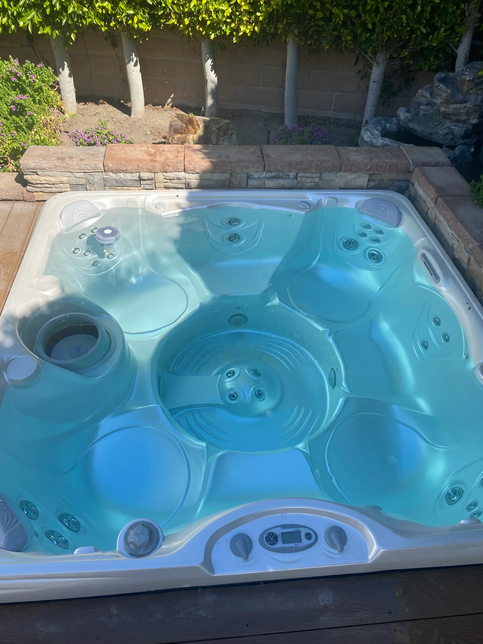 Blue hot tub with multiple jets and digital controls installed on wooden deck with stone surround