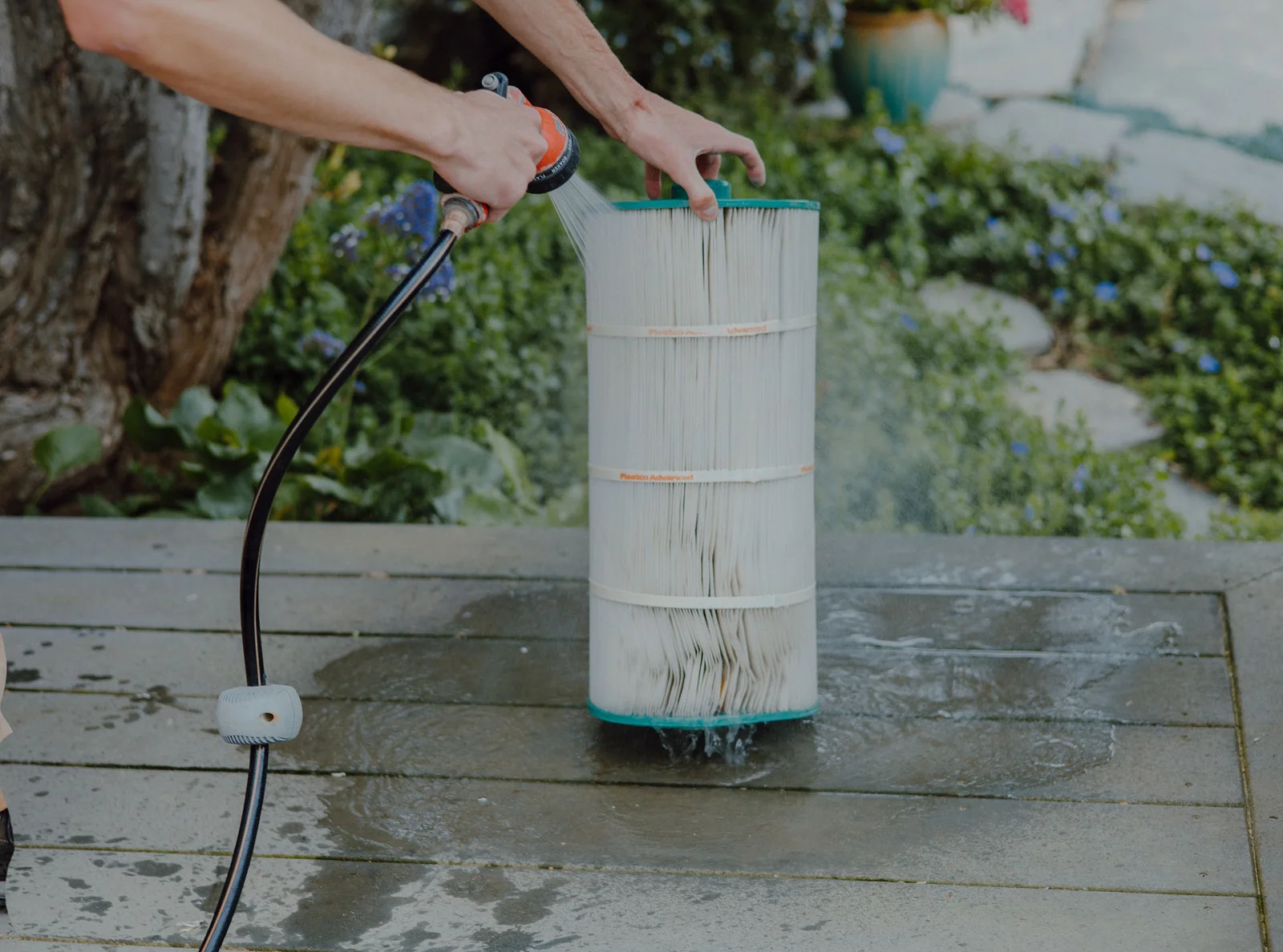 Technician rinsing pleated spa filter cartridge with pressurized water spray