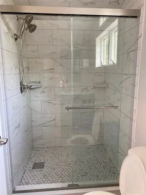 Frameless glass shower enclosure with chrome hardware, marble subway tile walls, and hexagonal mosaic floor
