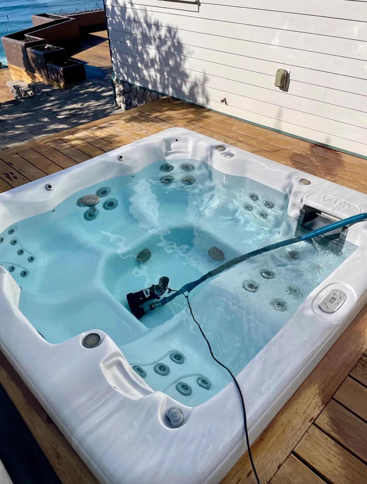 White acrylic hot tub with blue water and multiple jets being cleaned and serviced on wooden deck