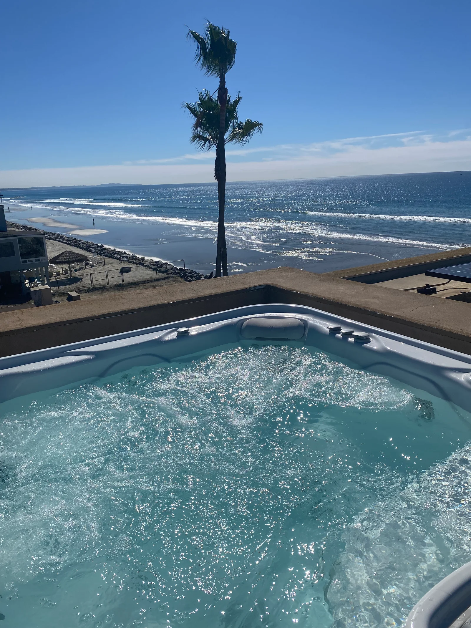 Fiberglass hot tub with jets and turquoise water on concrete deck overlooking beach