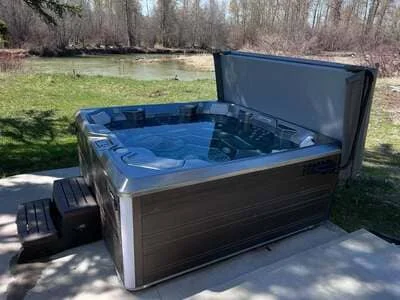 Dark composite hot tub with open cover showing interior basin and jet system in outdoor setting