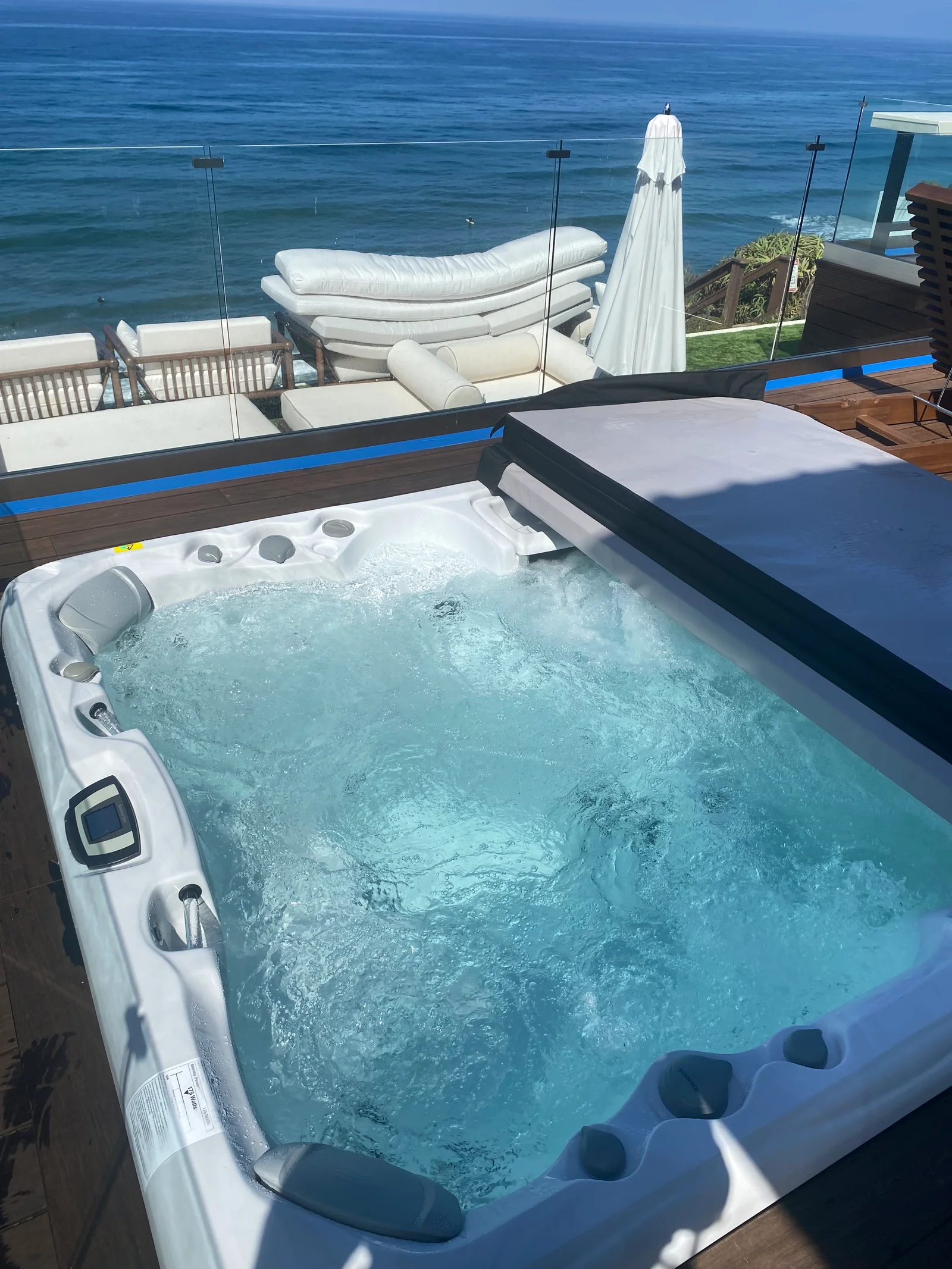 White hot tub with jets and seating on wooden deck overlooking ocean