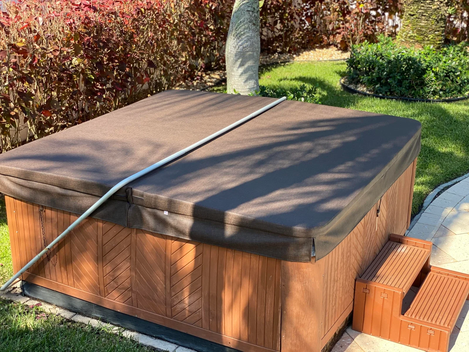 Dark gray hot tub cover with aluminum trim on cedar wood hot tub cabinet with wooden steps